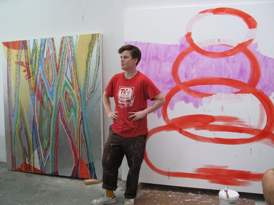 Artist Keltie Ferris in a red t-shirt, standing between two paintings