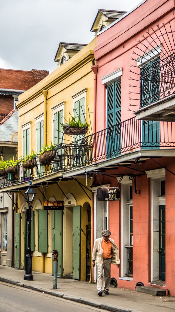 two colorful shop facades, one yellow with green shutters, and one pink with blue shutters, in the French Quarter of New Orleans