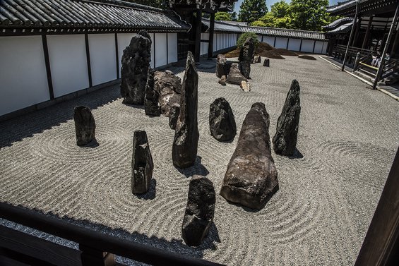 Garden at Tofuku-ji Temple in Kyoto with white pebbles raked into a swirling pattern around the base of large, dark, irregularly shaped standing rocks.