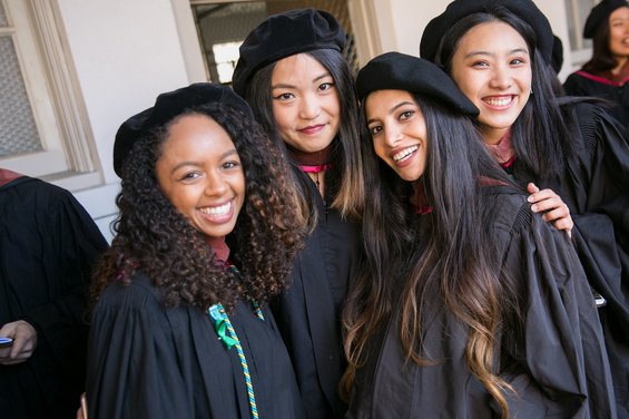 Color photo of four smiling students wearing traditional academic regalia.